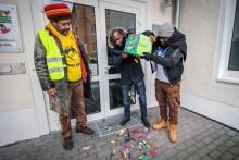 Auf der Oury Jalloh Demonstration 2018 schütten Mamadou Saliou Diallo, Bruder von Oury Jalloh, Mouctar Bah und Thomas Ndindah vor der Staatsanwaltschaft in Dessau Feuerzeuge aus, um auf das manipulierte Feuerzeug in Oury Jallohs Zelle hinzuweisen.