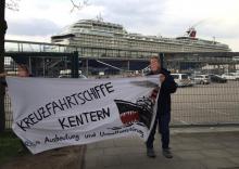 "Mein Schiff 1" hinter Transparent gegen Kreuzfahrtschiffe in Kiel