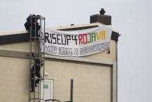 Cop klettert die Leiter zum Dach hoch, Rise up for Rojava Transpi sichtbar