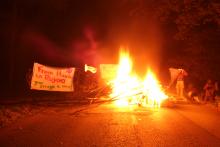 Solidarity photo for Rojava. A burning barricade, a banner wich says "From Hambi to Rojava your struggle is ours!" and a YPJ flag