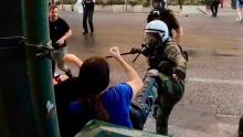 Foto/Videocut 28.7.2022: weiblich gelesene Person wehrt mit Arm den Tritt eines griechischen Bullen ab