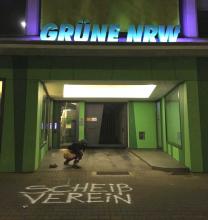 Mensch kackt vor dem Eingang der Landeszentrale der Grünen NRW, auf dem Boden steht "Scheißverein" gesprüht.