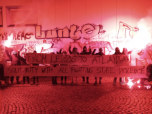 a gorup of anarchist holding some paper which states:"From leipzig to atlanta-solidarity with all fighting state violence" 2 Bengalos were burned.