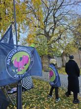 Echsen lauern auf Schwurbel im ländlichen Setting mit Masken vermummte mit Fahnen der "Antiverschwurbelten Aktion"