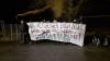 Eine Gruppe von Personen mit Rauchfackel und einem Transparent mit der Aufschrift "Wir vergessen euch nicht - Grüße an die Halloween-Gefangenen in der JA Linz! #linzwirdzuathena"