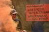 Im Vordergrund Pyrorauch, im Hintergrund ein Plakat mit der Aufschrift: entlassen, auslagern, prekarisierunge, PY Kultur?